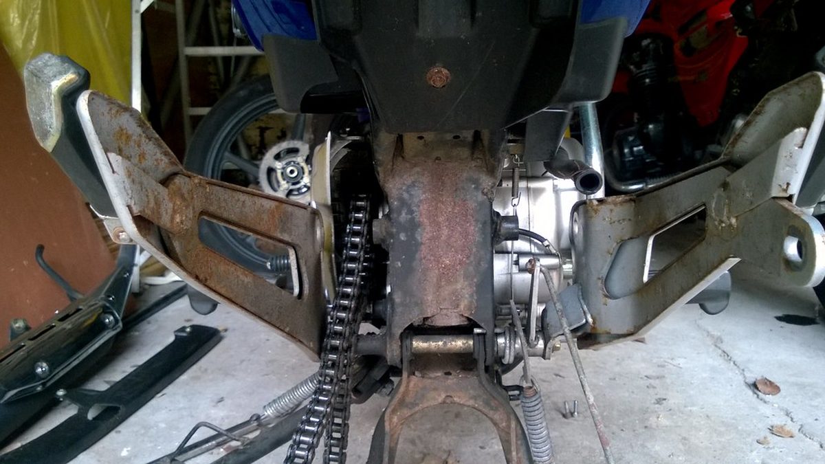 Catena e forcellone di una moto con evidenti segni di usura e ruggine